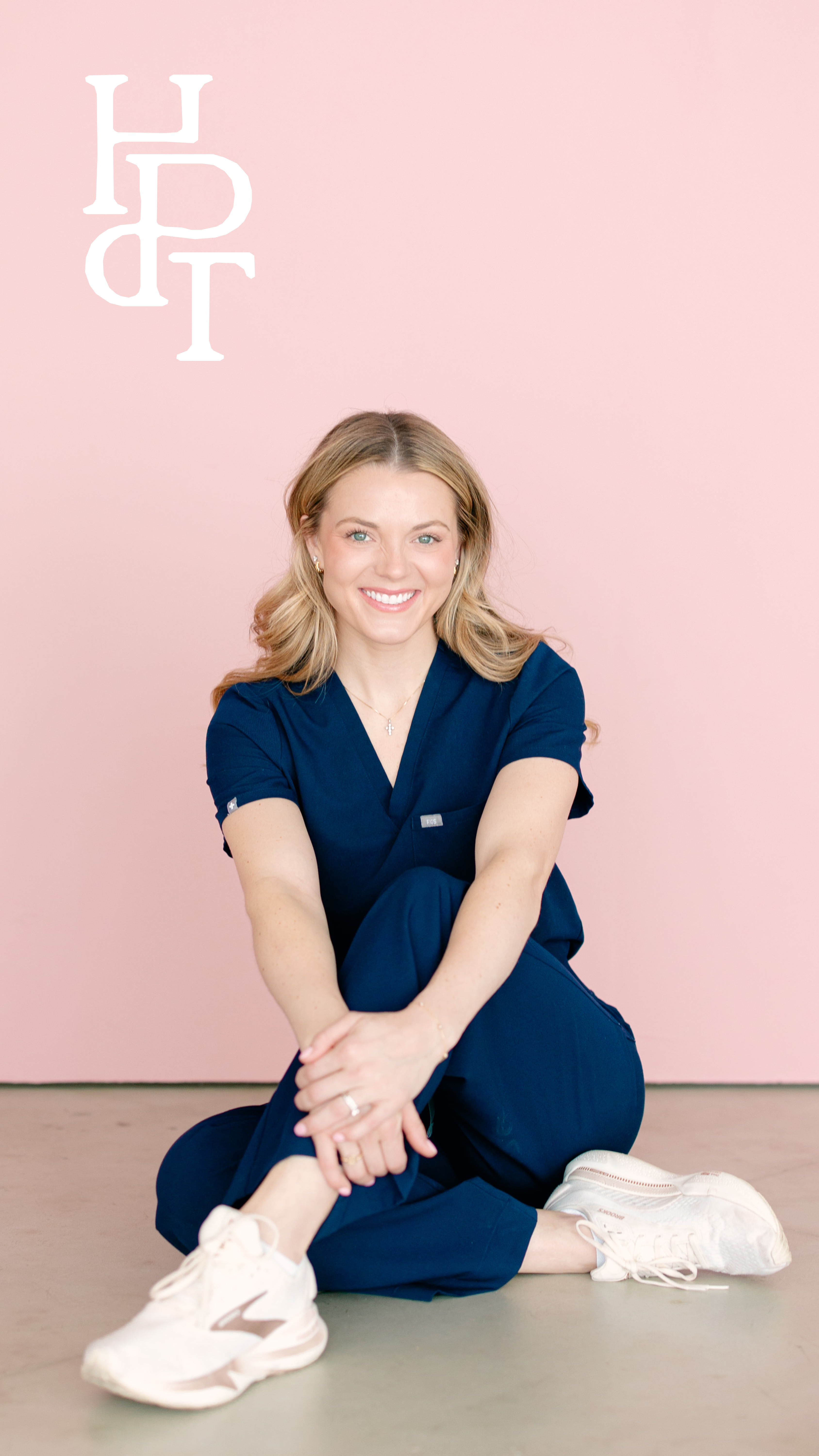Channing Stewart seated in navy scrubs against a pink background